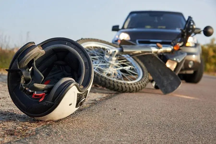 Motorcycle accident scene: a white helmet lies on the asphalt next to a crashed motorcycle, with a blurred car in the background. Safety gear and road safety are essential for all riders.